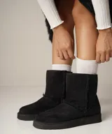 Bota de corderito negra con interior suave y diseño clásico, ideal para el frío.