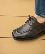 Zapato acordonado de cuero vacuno color marrón oscuro, con suela de goma, horma cuadrada y tacón bajo.