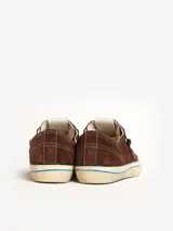 Zapatillas bajas marrones de gamuza con cordones negros, suela color crema con línea celeste y detalle de estrella calada en el lateral.