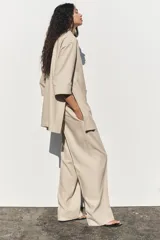 Pantalón color beige de lino, de tiro alto con cintura elástica, bolsillos laterales ocultos en costura y pernera ancha.