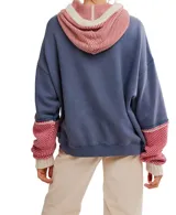 Hoodie oversized color azul desgastado con capucha y bolsillo canguro. Presenta un cuello y puños de tejido de punto con patrón a rombos en rojo y blanco, y cordones gruesos de color crema.