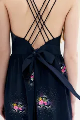 Vestido midi negro con estampado floral y puntos blancos. Presenta escote pronunciado en la espalda con múltiples tiras finas cruzadas que se atan con un lazo en la cintura.