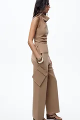 Top color beige de cuello halter y hombros descubiertos, con espalda descubierta, bajo con aberturas laterales y cierre en cuello con botones.
