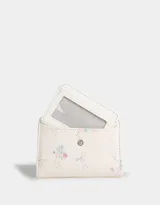 Billetera pequeña de cuerina color crema con estampado de flores y lazos. Tiene cierre superior y broche con botón para cerrar.