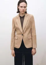Blazer color beige de gamuza, con cuello de solapa, cierre de un botón, dos bolsillos frontales con solapa, mangas largas con puños abotonados y forro interior.