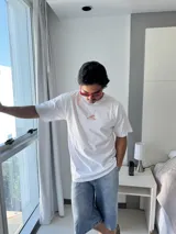 Remera blanca de manga corta con cuello redondo y corte holgado. Presenta un estampado gráfico en la espalda con elementos marinos (sol, ola, estrella de mar, flor, etc.) y el texto "VITAMIN SEA" y "BROKERS".