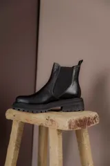 Bota Chelsea de cuero negro con elástico lateral y suela track.
