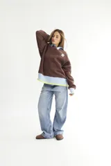 Buzo celeste con cuello polo y puños en rib color verde lima. Tiene un parche con el logo de la marca en el pecho y rayas horizontales en el ruedo.
