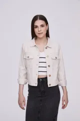 Campera corta color crudo, de corte recto, con cuello camisero, cierre frontal con botones color madera, mangas 3/4 con puños arremangados y bolsillos de parche en el pecho.