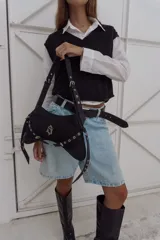 Cartera negra de gabardina y cuero, con correa regulable para usar al hombro. Tiene apliques metálicos plateados y logo colgante.