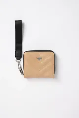 Billetera pequeña color beige con diseño capitoneado diagonal, cierre de cremallera y correa de mano negra.