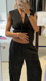 Pantalón negro con finas rayas verticales plateadas, de corte holgado y cintura con cordón ajustable.