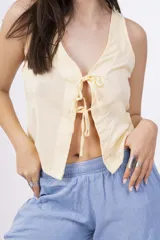 Chaleco corto sin mangas color verde salvia, confeccionado en tela perforada (broderie o calado). Presenta escote en V con lazos ajustables en el centro frontal.