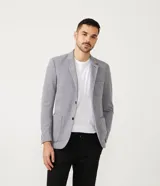Blazer masculino color gris claro, de tejido liso con textura casual, con solapas, bolsillos amplios de parche en la parte delantera y un bolsillo superior. Cierre frontal de un solo botón.