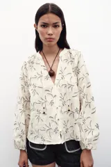 Blusa color crema con bordado floral en azul, de cuello redondo con cordón ajustable y mangas largas abullonadas con puños elásticos.