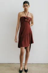 Vestido corto color borgoña, con escote halter, tiras para atar al cuello, falda irregular con volados y flor de lino con mostacillas en el escote.