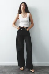 Pantalón de jean celeste de tiro alto, corte wide leg y largo hasta el tobillo. Presenta un diseño asimétrico en la cintura con cierre frontal cruzado con cremallera y botones metálicos.