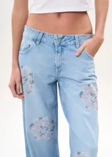 Pantalón de jean celeste de tiro bajo, corte wide leg y apliques de strass con forma de rosa en ambas piernas.