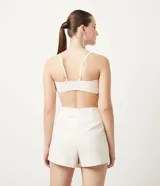 Musculosa cropped color crema, de material sintético, con tirantes finos ajustables, busto retorcido y elástico en el bajo.