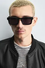 Cazadora bomber negra de tejido efecto piel, corte relajado, con cuello, puños y bajo en rib elástico a tono. Cierre frontal de cremallera y bolsillos de doble vivo en cadera.