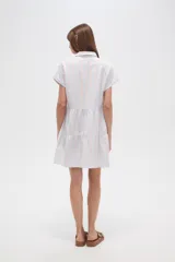 Vestido corto con cuello camisero, de corte holgado y mangas cortas. Presenta un diseño a rayas verticales en tonos beige y blanco, con volados en la falda y cierre frontal con botones.