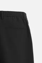 Pantalón negro de corte slim fit, confeccionado en tejido elástico. Cuenta con cintura elástica, bolsillos frontales y traseros de vivo. Cierre frontal con cremallera y botón.