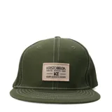 Gorro tipo snapback color verde oliva con visera plana y costuras blancas. Lleva un parche rectangular frontal de tela color beige con el texto "KRISTOBELGN ESTD. SINCE 1981" y el logo "KB SURF & SKATE GOODS".