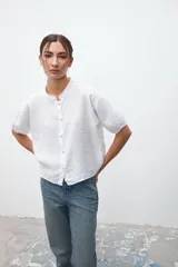 Camisa blanca de lino con cuello mao, manga corta abullonada y cierre frontal con botones.