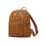 Mochila de lona revestida color marrón con monograma de la marca en toda la superficie, tachuelas metálicas doradas bordeando los bolsillos laterales, cierre bidireccional, asa superior reforzada, correas ajustables, dos compartimientos en la parte interior uno de ellos ideal para trasladar una tablet, bolsillos interior y exterior con cierre y placa metálica grabada con el nombre de la marca en la parte frontal.