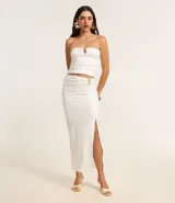 Conjunto de dos piezas color blanco, compuesto por un top tipo corset strapless con escote en V y una pollera midi ajustada con fruncido lateral y abertura alta, asegurada con un adorno metálico.