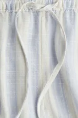 Pantalón de tiro bajo con elástico y cordón ajustable en la cintura, bolsillos al bies y piernas rectas. Confeccionado en tejido liviano con lino en la trama y estampado a rayas verticales en tonos celeste y beige.
