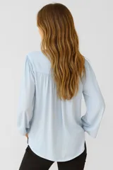 Blusa celeste de viscosa con cuello en V y mangas largas. Presenta detalles de broderie en los hombros y corte holgado.