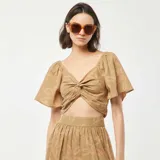 Conjunto de blusa cropped y falda midi con estampado de hojas en tonos rosados sobre fondo verde. La blusa tiene escote en V, mangas cortas tipo mariposa y un lazo decorativo en el frente. La falda es de corte evasé.