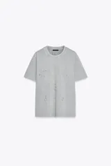 Camiseta gris de algodón con cuello redondo y manga corta. Tiene apliques de strass plateado en el frente.