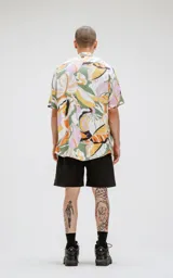 Camisa de manga corta con estampado de hojas en tonos naranja, verde y rosa sobre fondo blanco. Corte oversize.