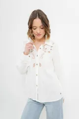 Camisa blanca de voile con bordados calados en el frente, cuello camisero, mangas largas con puños abotonados y cierre frontal con botones. 