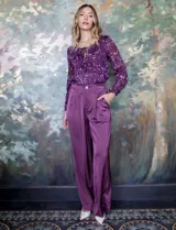 Pantalón palazzo de tiro alto color violeta, de satén. Tiene pretina delantera con pasadores, botón y cierre, pretina trasera elastizada y bolsillos verticales delanteros.