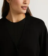 Chaqueta corta de punto color negro, con escote en V, manga larga abullonada, sisa desplazada, abotonado frontal total con botones forrados y puños acanalados.