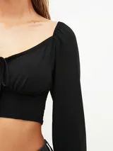Blusa crop top negra con escote cuadrado, mangas largas abullonadas y lazo ajustable en el centro del busto.