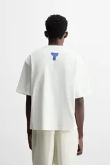 Camiseta blanca de corte regular fit, cuello redondo y manga corta. Presenta parches geométricos combinados a contraste en el delantero y estampado en la espalda.
