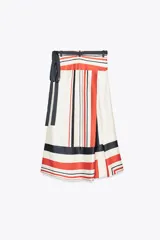 Falda midi de tiro medio con estampado de rayas rojas, negras y blancas. Tiene bajo asimétrico y cierre frontal tipo pareo ajustable con lazos negros.