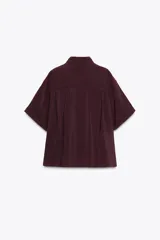 Camisa color borgoña de corte amplio, confeccionada en tejido fluido con modal. Tiene cuello solapa, manga corta con dobladillo y cierre frontal con botones.