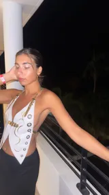 Top de cuero blanco con detalles dorados, diseño asimétrico y cierre frontal con hebilla.