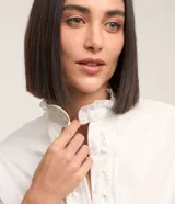 Camisa blanca de tricolina con cuello padre, abotonada al frente con detalle ondulado y mangas largas.
