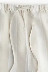 Short de lino y viscosa color crudo con rayas verticales en tono beige. Tiene cintura elástica con cordón ajustable y bolsillos laterales.