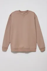 Sudadera de tejido liso color beige, con cuello redondo y puños y ruedo acanalados. Se lleva superpuesta a una camisa de cuadros celestes y blancos.