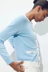 Chaqueta celeste de punto con cuello redondo y manga larga. Tiene cierre frontal con botones y detalle de falsos bolsillos delanteros con ribete blanco.