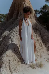 Vestido largo de calce fluido, color blanco, con escote en V profundo y tiras largas que permiten múltiples formas de atar el cuello. Posee tajos laterales y forro interno.