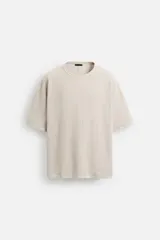 Camiseta color arena de punto tejido en hilatura de algodón, con cuello redondo, manga corta, efecto lavado y acabados irregulares.