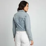 Chaqueta de jean celeste de corte cropped, con cuello clásico, cierre frontal con botones metálicos, bolsillos de parche con solapa en el pecho y mangas largas con puños abotonados.
